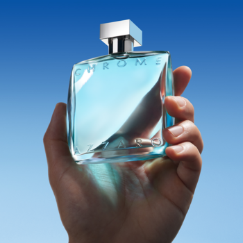 Azzaro Chrome męska woda toaletowa w szklanej butelce z jasnoniebieskim płynem, trzymana w dłoni na błękitnym tle.