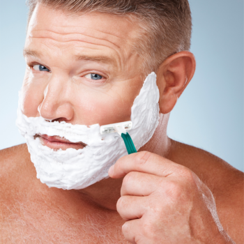 Mężczyzna goli się jednorazową golarką BIC Comfort 2 z zieloną rączką, twarz pokryta białą pianką.