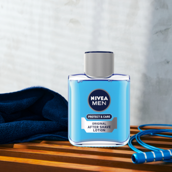 NIVEA MEN Protect & Care, błękitna woda po goleniu w szklanej butelce, na drewnianym blacie z ręcznikiem.