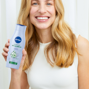 Uśmiechnięta kobieta trzyma butelkę NIVEA Moisture Hyaluron Szampon nawilżający z hialuronem, widok z przodu.