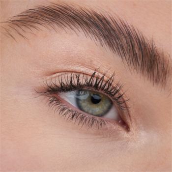 Zbliżenie na oko modelki z długimi rzęsami i ułożoną brwią, widoczny efekt rozświetlacza Catrice All Over Glow Tint.
