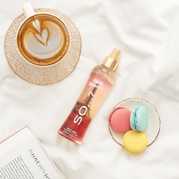 So...? Paris Romance mgiełka do ciała z Wieżą Eiffla, kawa latte, makaroniki, książka. Flat lay na białej pościeli.