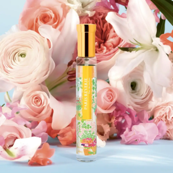 Adopt Paris Rêverie Eau de Parfum w smukłej butelce z żółtą nakrętką, wśród bukietu pastelowych kwiatów.