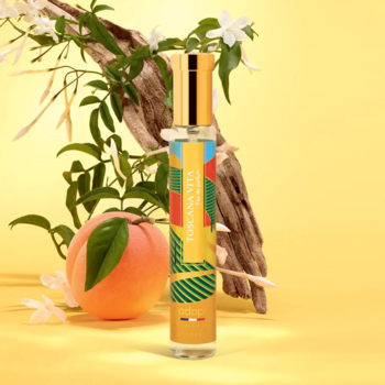Adopt Toscana Vita perfumy, smukła złota butelka z kolorową etykietą, na żółtym tle z brzoskwinią i jaśminem.