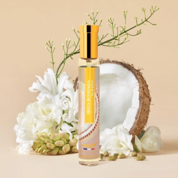 Adopt Ibiza Bohemia, złota woda perfumowana w smukłej butelce, otoczona kokosem i białymi kwiatami na beżowym tle.