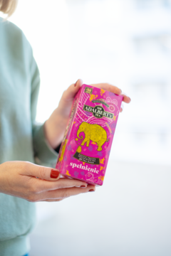 Różowe opakowanie herbaty Adalbert's Tea Exotic Fruits SPEŁNIENIE ze złotym słoniem, w dłoniach.