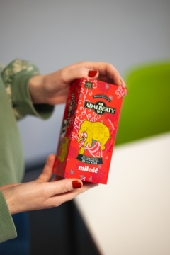 Czerwone opakowanie herbaty Adalbert's Tea Strawberry MIŁOŚĆ trzymane w dłoniach, z grafiką żółtego słonia.