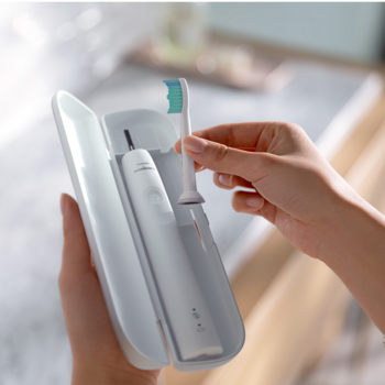 Zbliżenie na dłonie wkładające zieloną końcówkę do białego etui ze szczoteczką soniczną Philips Sonicare.