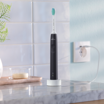 Czarna szczoteczka soniczna Philips Sonicare z niebieską główką, na białej ładowarce w łazience.