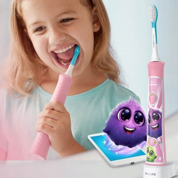 Dziewczynka szczotkuje zęby różową soniczną szczoteczką Philips Sonicare For Kids, z tabletem i fioletowym stworkiem z aplikacji.