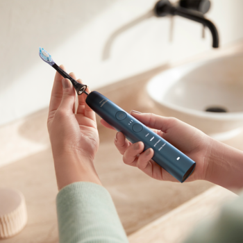 Dłonie trzymają ciemnoniebieską szczoteczkę soniczną Philips DiamondClean 9000, do bielszych zębów.