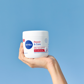 Biały krem NIVEA Repair & Care w słoiku, trzymany w dłoni na tle błękitnego nieba, intensywne nawilżenie.