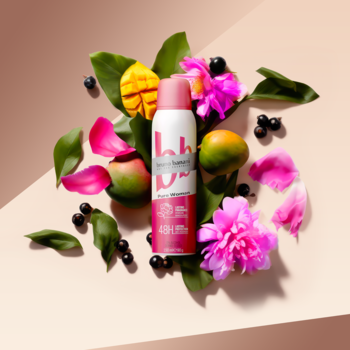 Dezodorant Bruno Banani Pure Woman 48H z mango i piwonią, różowy spray wśrodku owoców i kwiatów.