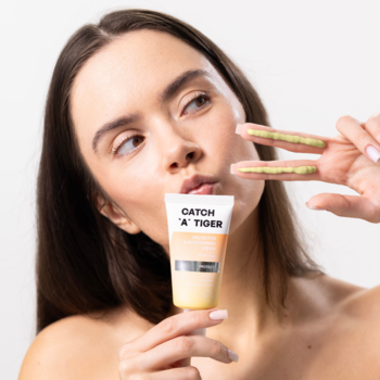 Kobieta trzyma krem SPF 50 Catch A Tiger; na palcach oliwkowy krem do twarzy. Nawilżający krem redukujący zaczerwienienia.