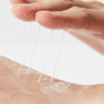 Zbliżenie na Cosrx Advanced Snail Peptide krem ze śluzem ślimaka, z ciągnącą konsystencją rozciąganą między palcami.