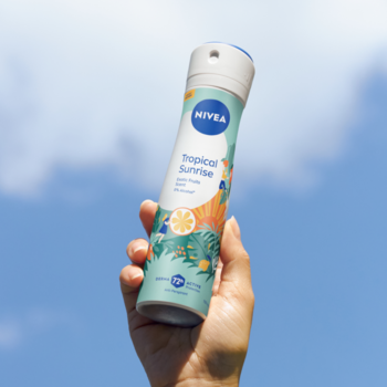Antyperspirant NIVEA Tropical Sunrise w białym sprayu z pomarańczowo-zielonym wzorem, trzymany pod niebem.