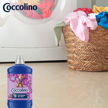 Coccolino Purple Orchid & Blueberries płyn do płukania. Niebieska butelka na pierwszym planie, w tle pranie w pralce.