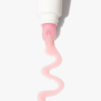 Blady różowy olejek do ust Marshmallow Glow wypływa z białej tubki, tworząc lśniącą, falistą smugę.