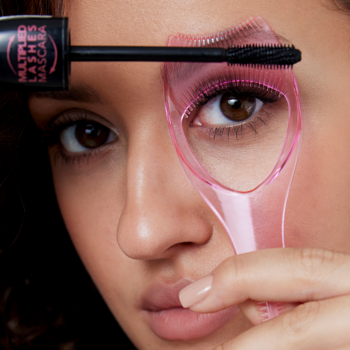 Zbliżenie na kobietę używającą różowej osłonki Donegal do rzęs z grzebykiem. Aplikator chroni powiekę przed tuszem.