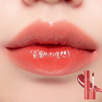 Zbliżenie na usta pokryte Rom&nd Juicy Lasting Tint 07, błyszczyk w odcieniu koralowym, z lustrzanym połyskiem.