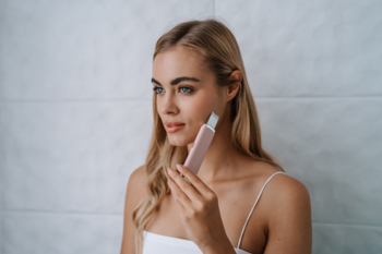 Blondynka używa różowego B-Scrub PRO Slim do peelingu kawitacyjnego twarzy, na białym tle, poprawia jędrność skóry.