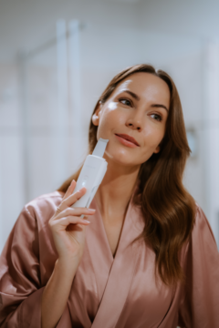 Kobieta w różowym szlafroku, używa białego Beautifly Scrub Aqua Glow PRO do peelingu kawitacyjnego na policzku.