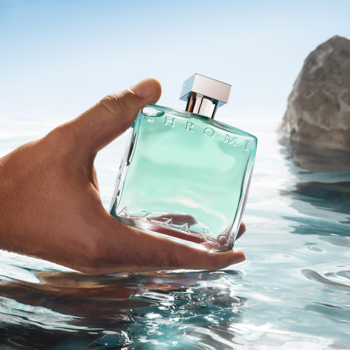 Flakon Azzaro Chrome Azure EDT o błękitno-zielonej barwie w męskiej dłoni, zanurzony w wodzie. Świeży, morski zapach.