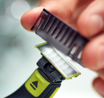 Zbliżenie na dłoń mocującą ciemny grzebień do strzyżenia do trymera Philips OneBlade QP2724-23 w kolorze limonkowym.