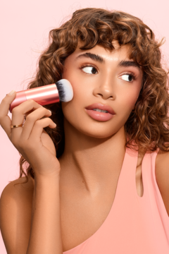 Modelka używa pędzla Real Techniques Bubble Blending Brush z różowo-złotą rączką do blendowania na policzku.