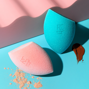 Duo gąbek Real Techniques Miracle Mattifying: różowa i turkusowa, z pudrem i podkładem na dwukolorowym tle.