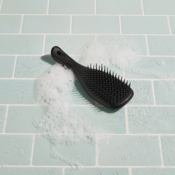 Czarna szczotka Tangle Teezer z rączką do rozczesywania włosów, na mokrych turkusowych płytkach z pianą.