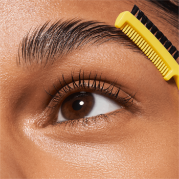 Zbliżenie oka, laminowana brew stylizowana żółtym grzebykiem wosku Catrice Brow Sleek Laminating Wax.
