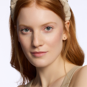 Zbliżenie na rudowłosą modelkę z promienną cerą, ukazującą naturalne rozświetlenie z Catrice Holiday Skin.