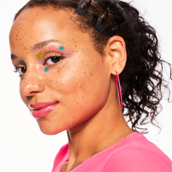 Modelka z aplikowanym rozświetlaczem Baby Got Holo Glow, kolorowe punkty wokół oka tworzą holograficzny blask.