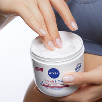 Dłonie nabierają nawilżający krem NIVEA Repair & Care Urea z białego pojemnika, dla suchej skóry ciała i twarzy.