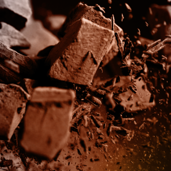 Zbliżenie na nieregularne, ciemne kawałki czekolady i okruchy, symbolizujące zapach Axe Dark Temptation dezodorantu.