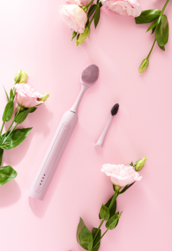 Różowa szczoteczka soniczna Seysso Basic Color Misty Rose 2w1 do zębów i twarzy, z wymienną końcówką, na różowym tle z kwiatami.