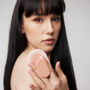 Kobieta trzyma różową owalną myjkę silikonową Donegal do twarzy i ciała, z widoczną dwuczęściową budową.