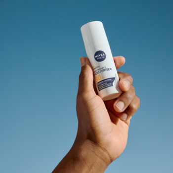 Biała butelka NIVEA MEN Sensitive Triple Protect krem nawilżający SPF30 trzymana w dłoni na tle błękitnego nieba.