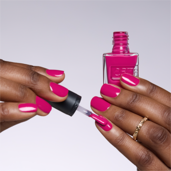 Dłonie aplikujące żelowy lakier Catrice Gel Affair Berry Styles. Jaskrawy fuksjowy kolor, widoczna butelka i pędzelek.