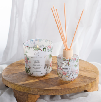 Świeca zapachowa Exotic Flowers i dyfuzor Aroma Home w szklanych naczyniach z tropikalnym wzorem, na drewnianej tacy.
