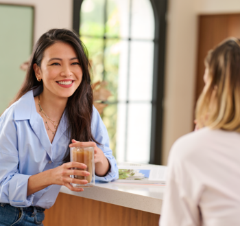 Uśmiechnięta kobieta z kawą, prezentuje białe zęby dzięki Philips Sonicare W2 Optimal White.