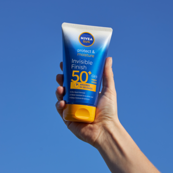 Nivea Sun Protect & Moisture SPF 50+ w żółto-niebieskiej tubce, trzymany ręką na tle błękitnego nieba.