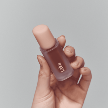 Laka Fruity Glam Tint Humming, błyszcząca pomadka w płynie, w matowej butelce, trzymana w dłoni. Zbliżenie.