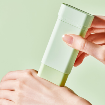 Zbliżenie dłoni aplikującej jasnozielony Tocobo Cica Cooling Sun Stick SPF 50+ na przedramię na zielonym tle.