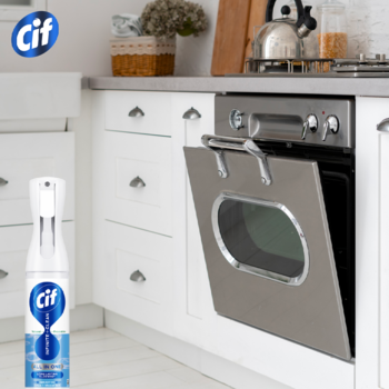 Biała butelka sprayu Cif Infinite+ Clean do czyszczenia, w kuchni obok szafek i piekarnika.