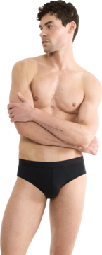 Mężczyzna bez koszulki w czarnych slipach Sloggi Men Core Comfort Brief, ręce skrzyżowane, patrzy w lewo.