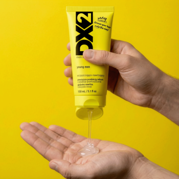 Żółta tubka szamponu DX2 Young Men wyciskana na otwartą dłoń, przezroczysty żel, tło żółte.