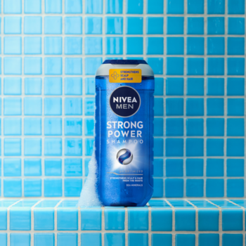 Niebieski szampon NIVEA MEN Strong Power z minerałami morskimi, na tle błękitnych kafelków prysznicowych.