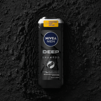 Czarna butelka NIVEA MEN Deep Szampon z czarnym węglem, z niebieskim logo, na tle ciemnego proszku. Widok z góry.